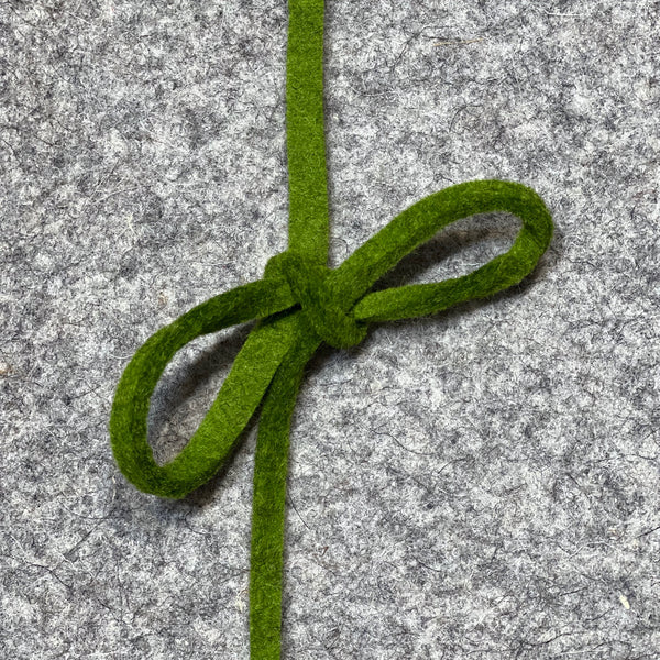 Image shows green bow tied on a piece of grey felt - as it might be used as a gift.
